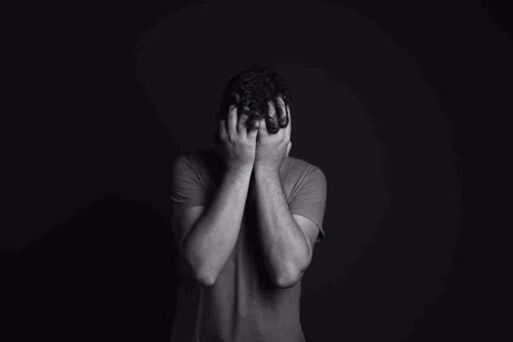 A grayscale portrait of a man covering his face, depicting emotion and mental health themes.